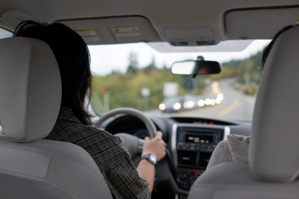 Joven conduciendo un turismo por carretera, vista desde el asiento trasero